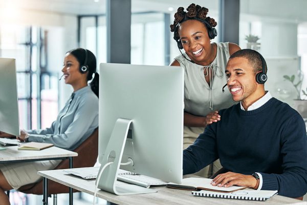 Support, training and coaching, a call center manager is happy to help her team. Collaboration, leadership and teamwork at a tech startup. Office diversity, young men and women working with computers